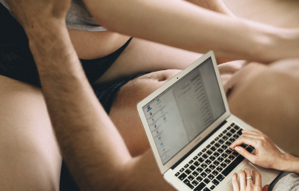 a partially clothed man and woman with a writer's hands on a notebook computer to illustrate the blog Writing Sexy Memoir Scenes
